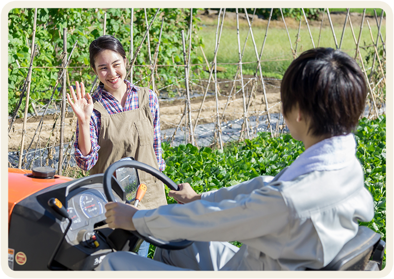 畑でトラクターを運転する人と手を振る女性